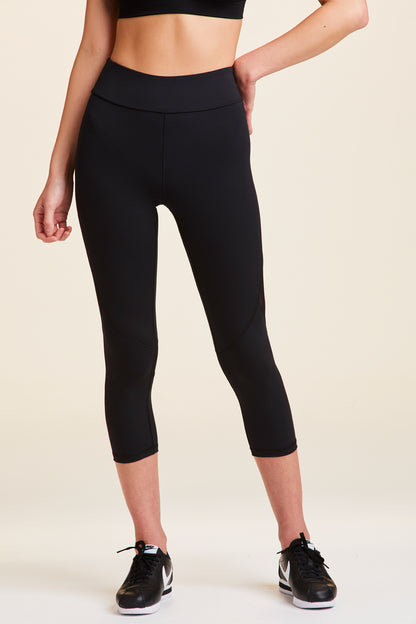 Front view of Alala Women's Luxury Athleisure cropped black tight with mesh paneling on back of knees.