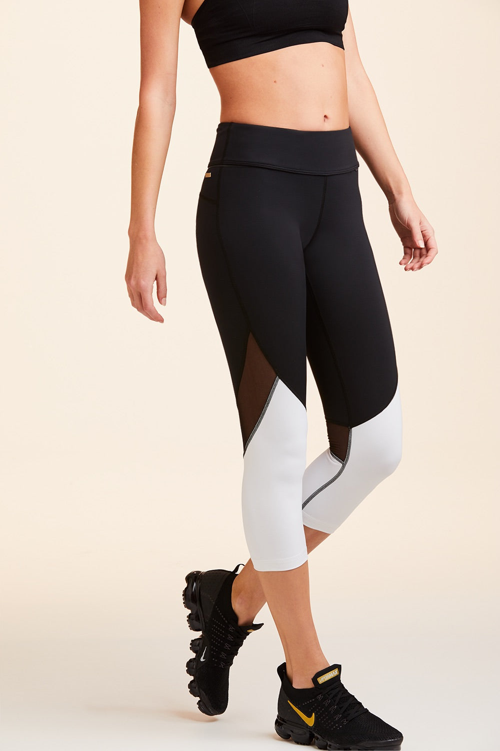 Side view of Alala Women's Luxury Athleisure cropped black and white tight with mesh paneling on back of knees.