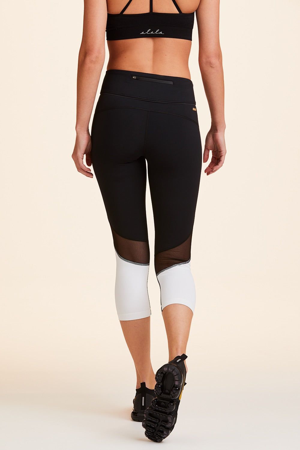 Back view of Alala Women's Luxury Athleisure cropped black and white tight with mesh paneling on back of knees.