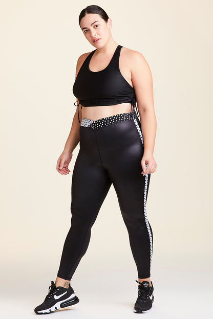 3/4 view of Alala Women's Luxury Athleisure shiny black tight with black and white polda dot detail on waistband and side seams in plus size