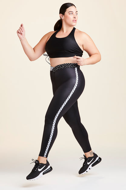 Side view of Alala Women's Luxury Athleisure shiny black tight with black and white polda dot detail on waistband and side seams in plus size