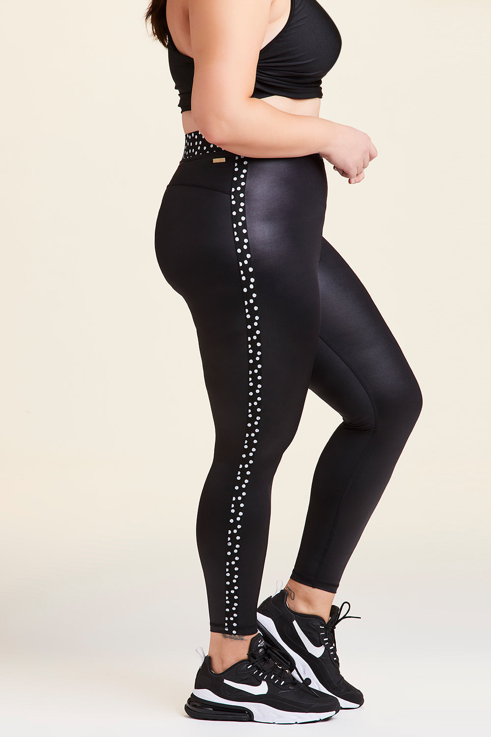 Side view of Alala Women's Luxury Athleisure shiny black tight with black and white polda dot detail on waistband and side seams in plus size