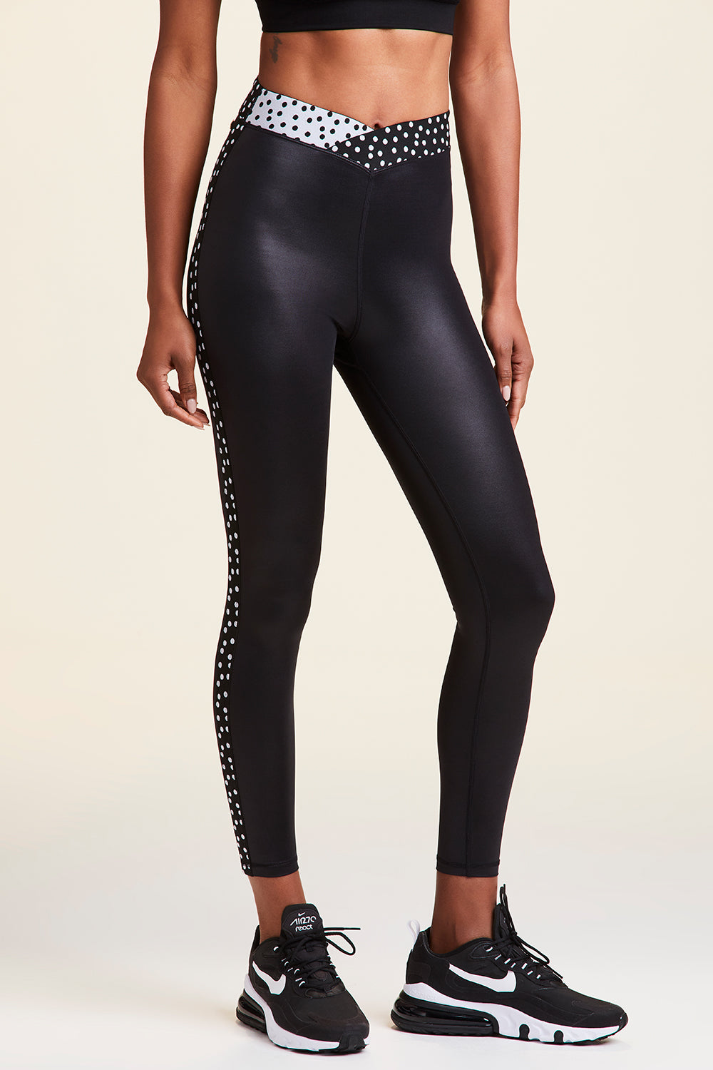 Front view of Alala Women's Luxury Athleisure shiny black tight with black and white polda dot detail on waistband and side seams
