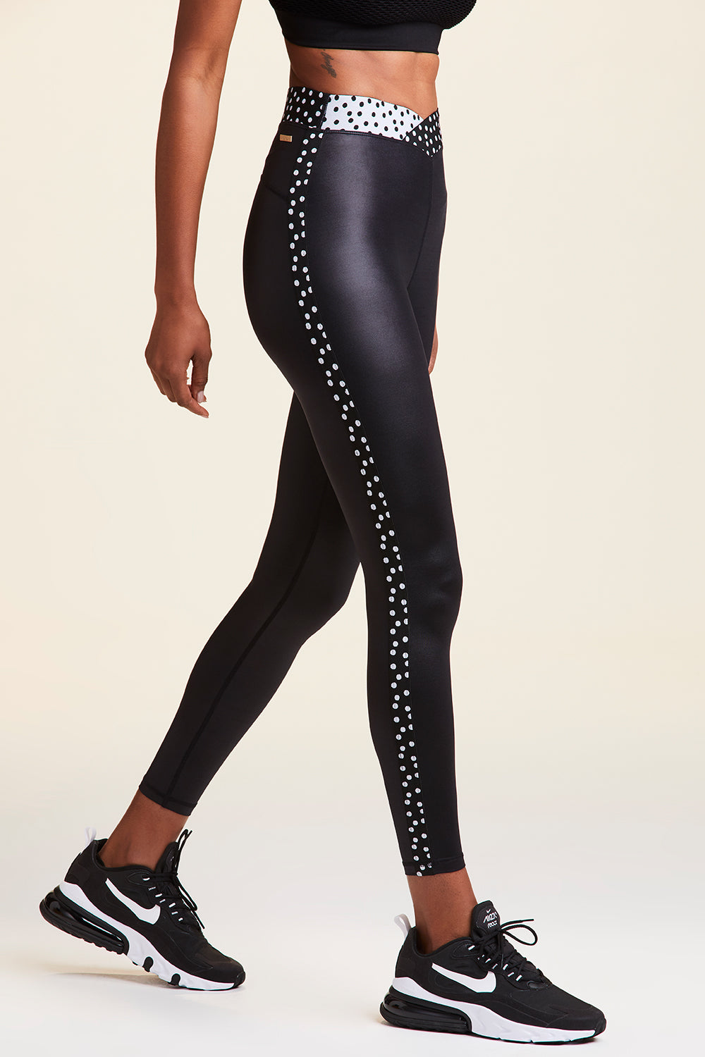 Side view of Alala Women's Luxury Athleisure shiny black tight with black and white polda dot detail on waistband and side seams