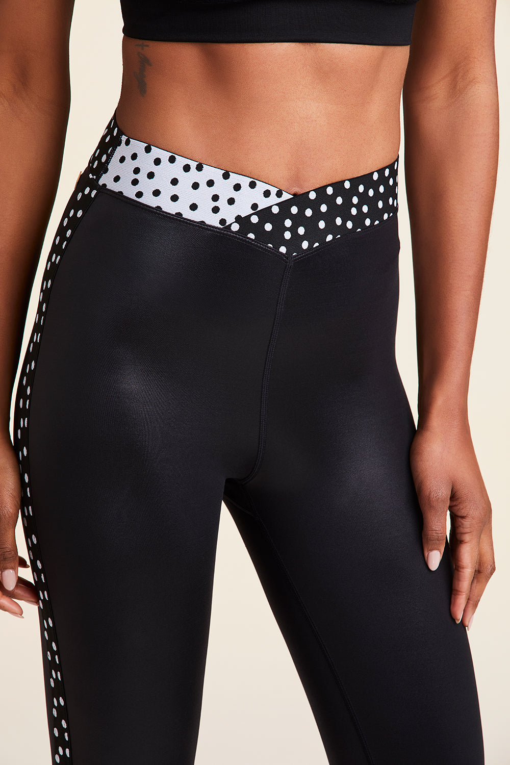 Front close-up view of Alala Women's Luxury Athleisure shiny black tight with black and white polda dot detail on waistband and side seams