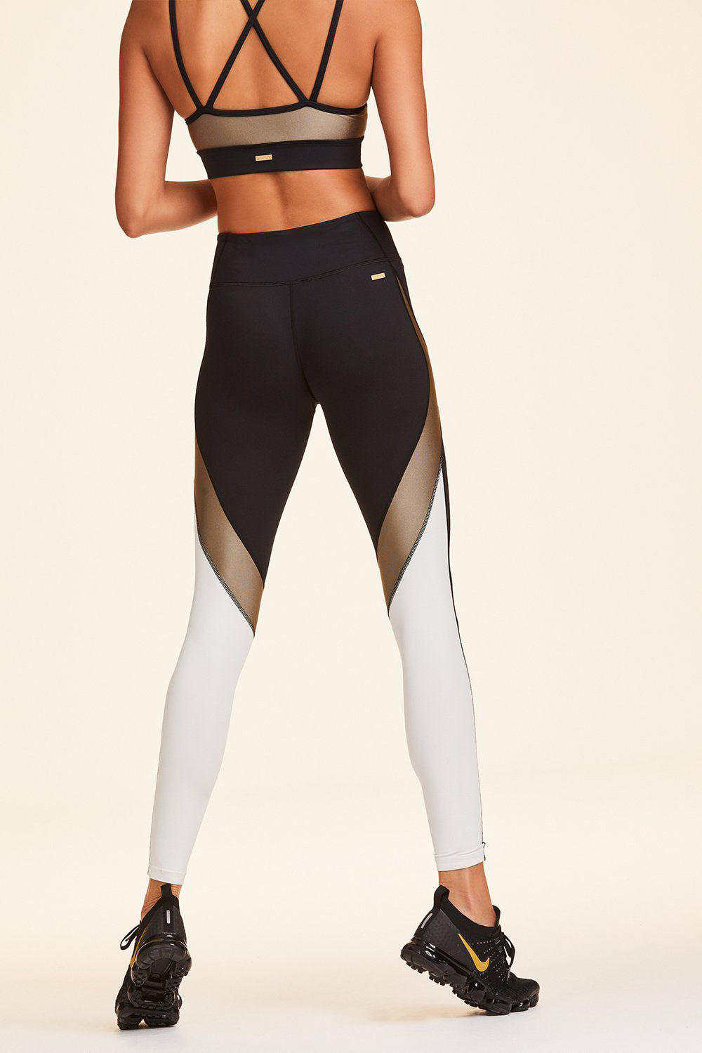 Back view of Alala Women's Luxury Athleisure black, white, and gold color-blocked tight
