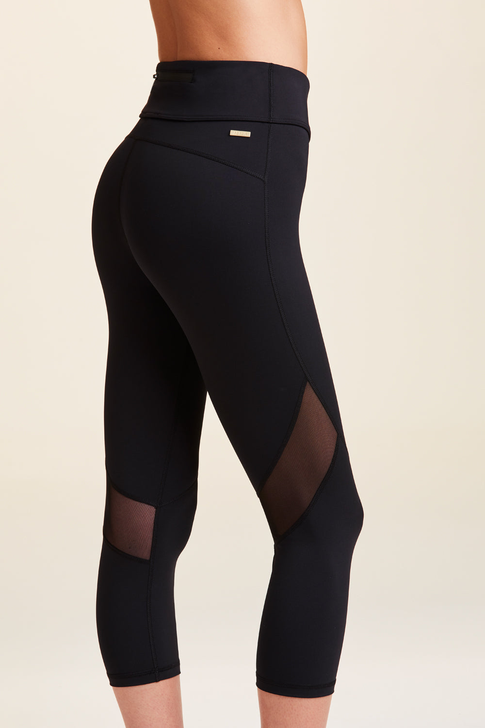 Side view of Alala Women's Luxury Athleisure cropped black tight with mesh paneling on back of knees.
