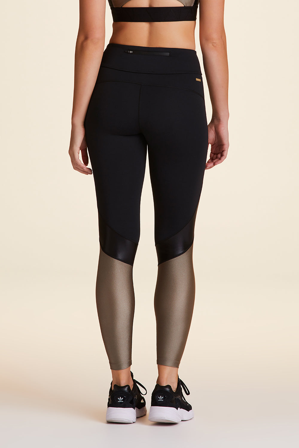 Back view of Alala Luxury Women's Athleisure captain ankle tight in black and gold dust