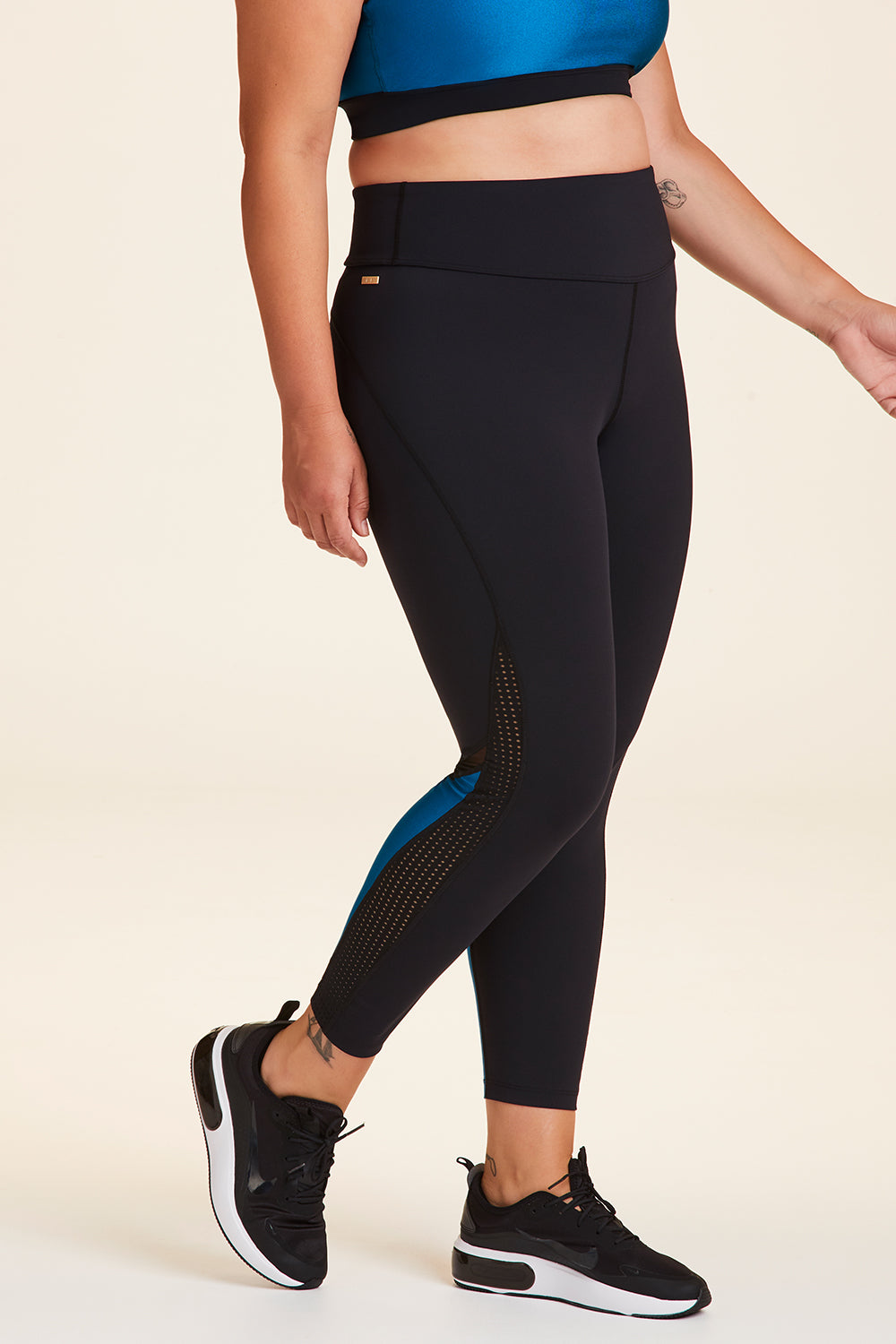Side view of Alala Women's Luxury Athleisure black and teal 7/8 tight with minimal mesh detail in plus size