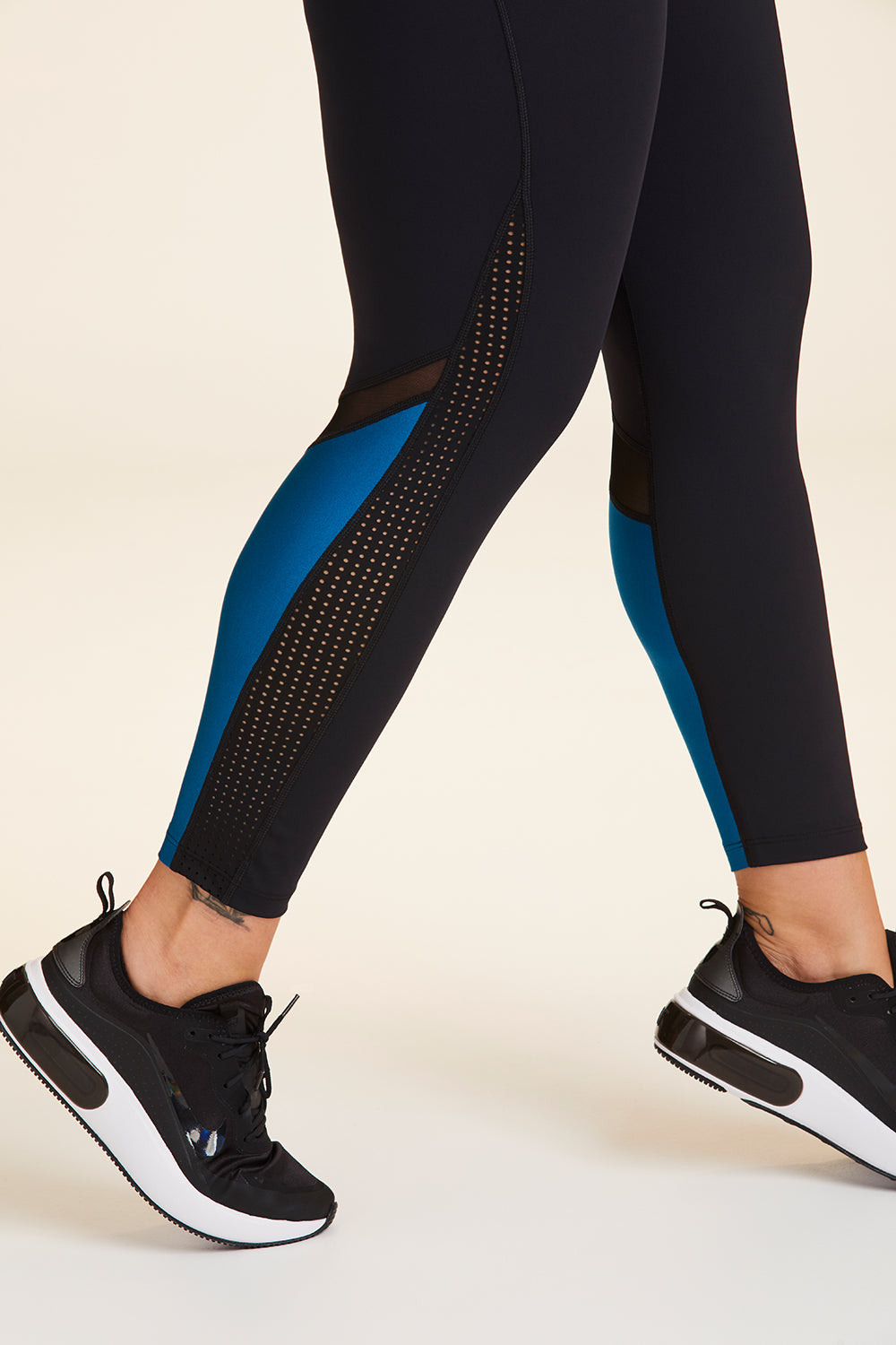 Side view close-up of Alala Women's Luxury Athleisure black and teal 7/8 tight with minimal mesh detail in plus size